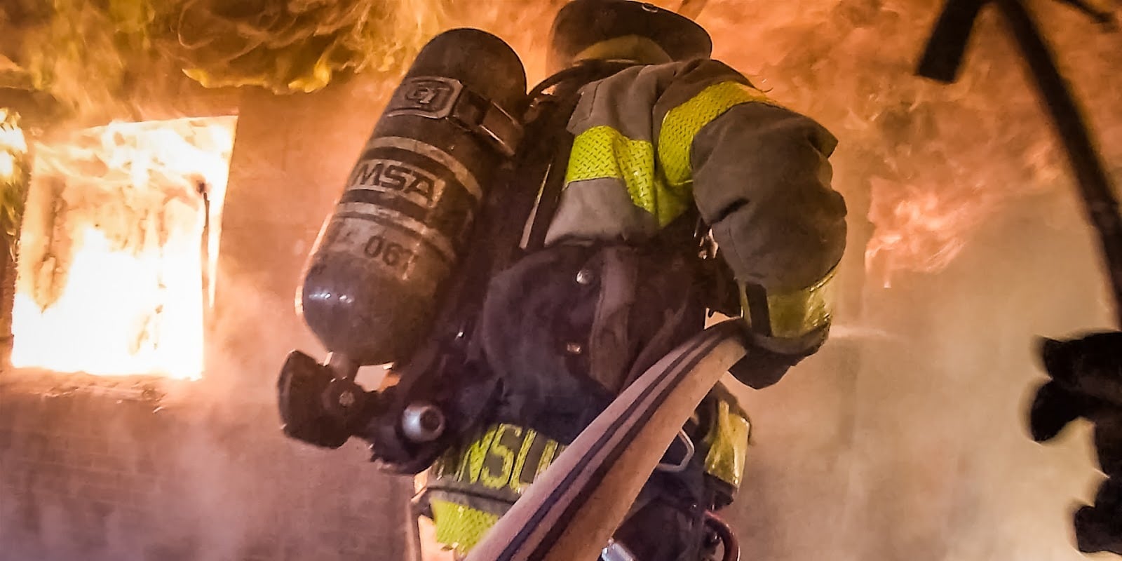 Firefighter advances a hose line through a burning structure.